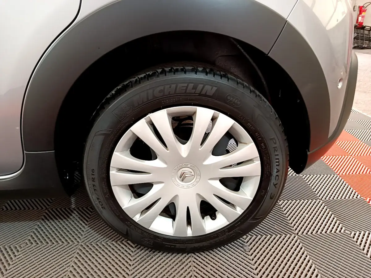 Gros plan sur la roue avant droite d'une Citroën C3 gris clair, avec jante acier et enjoliveur blanc éclatant.