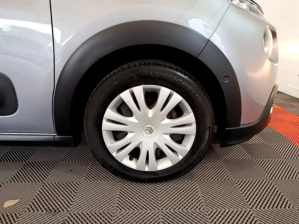 Gros plan sur la roue avant droite d'une Citroën C3 gris clair avec jante acier et enjoliveur blanc.