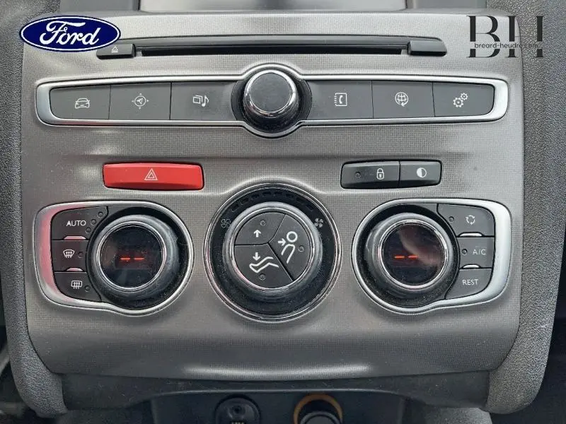 Tableau de bord avec commandes climatisation et boutons multifonctions d'une Citroën C4 blanche, vue intérieure frontale.