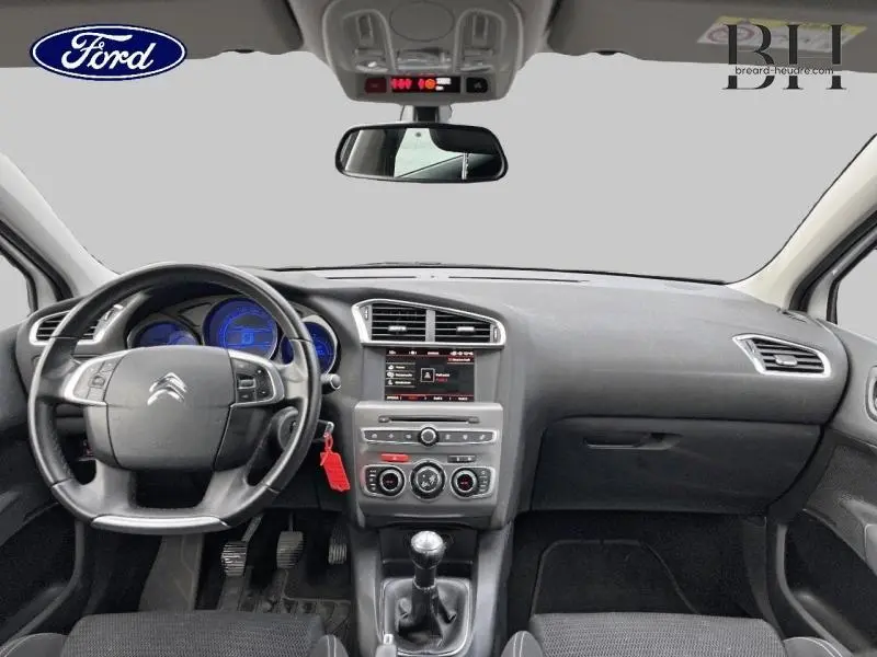 Vue intérieure avant du tableau de bord et volant noir d'une Citroën C4 blanche, avec boîte manuelle et écran central.