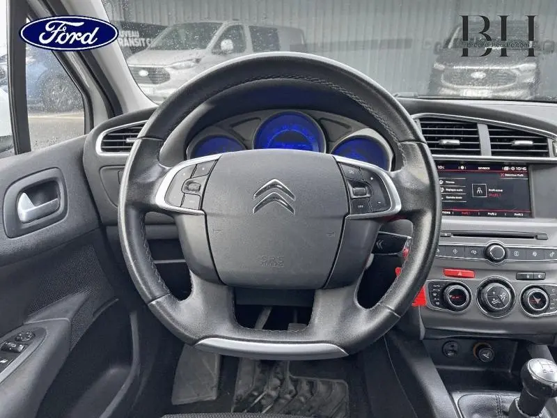 Vue intérieure centrée sur le volant noir de la Citroën C4 blanche de 2017 avec tableau de bord et console centrale visibles.