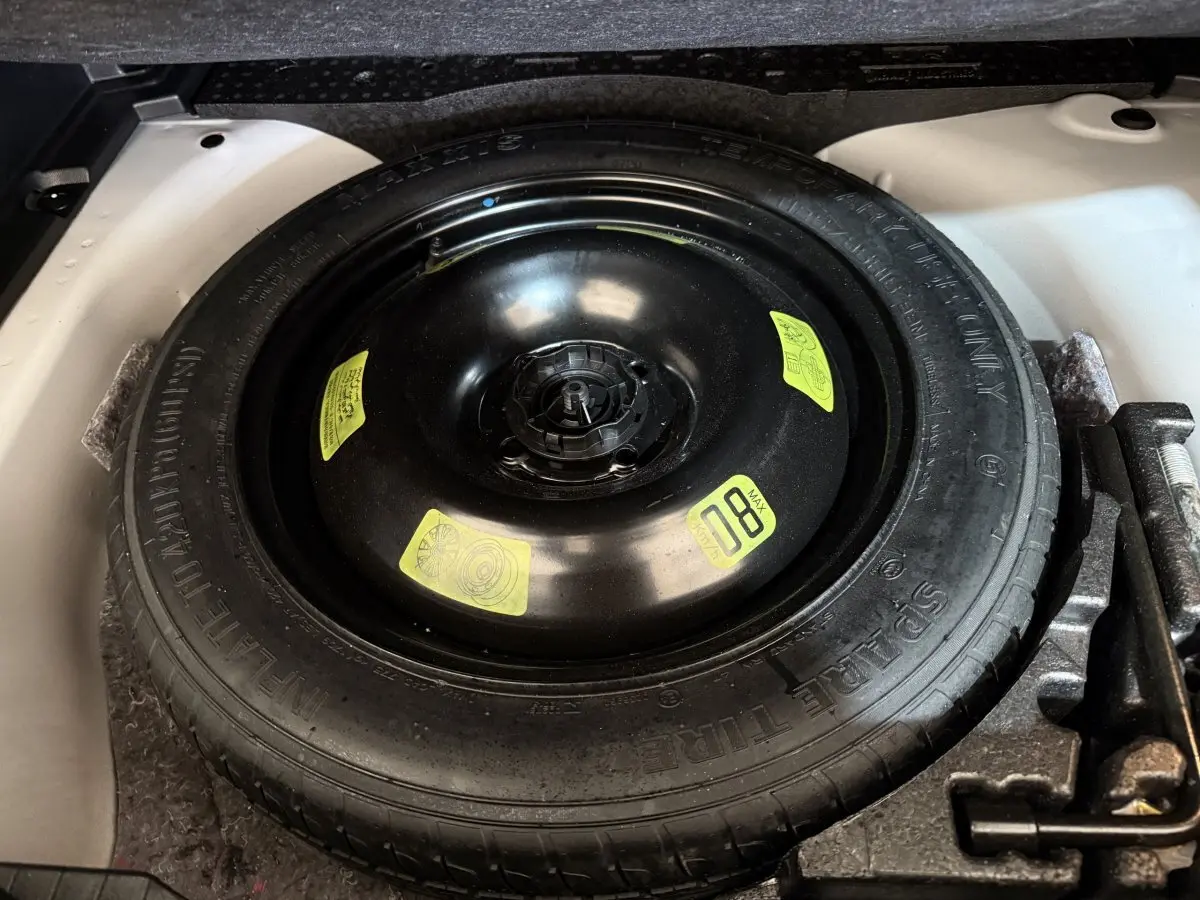Vue rapprochée de la roue de secours noire dans le coffre blanc d’un Peugeot 2008 BlueHDi 130 de 2021.