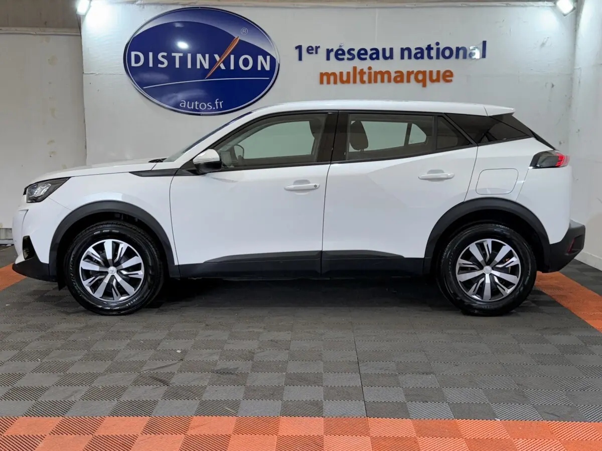 Peugeot 2008 blanc vue de profil côté gauche, avec jantes alliage et toit noir contrastant en intérieur showroom.