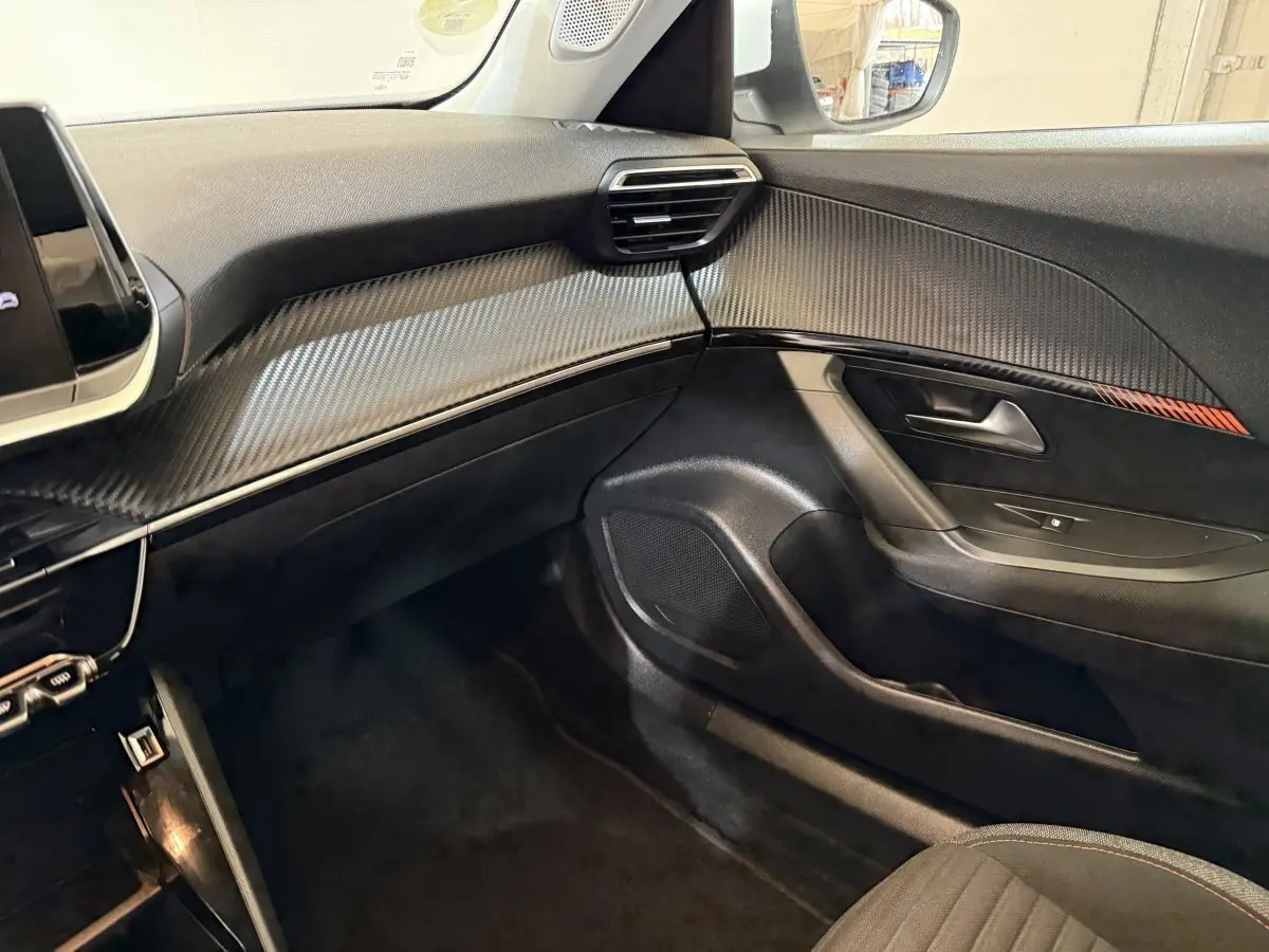 Vue intérieure côté passager du Peugeot 2008 2021, tableau de bord noir avec insert effet carbone et détails rouges.