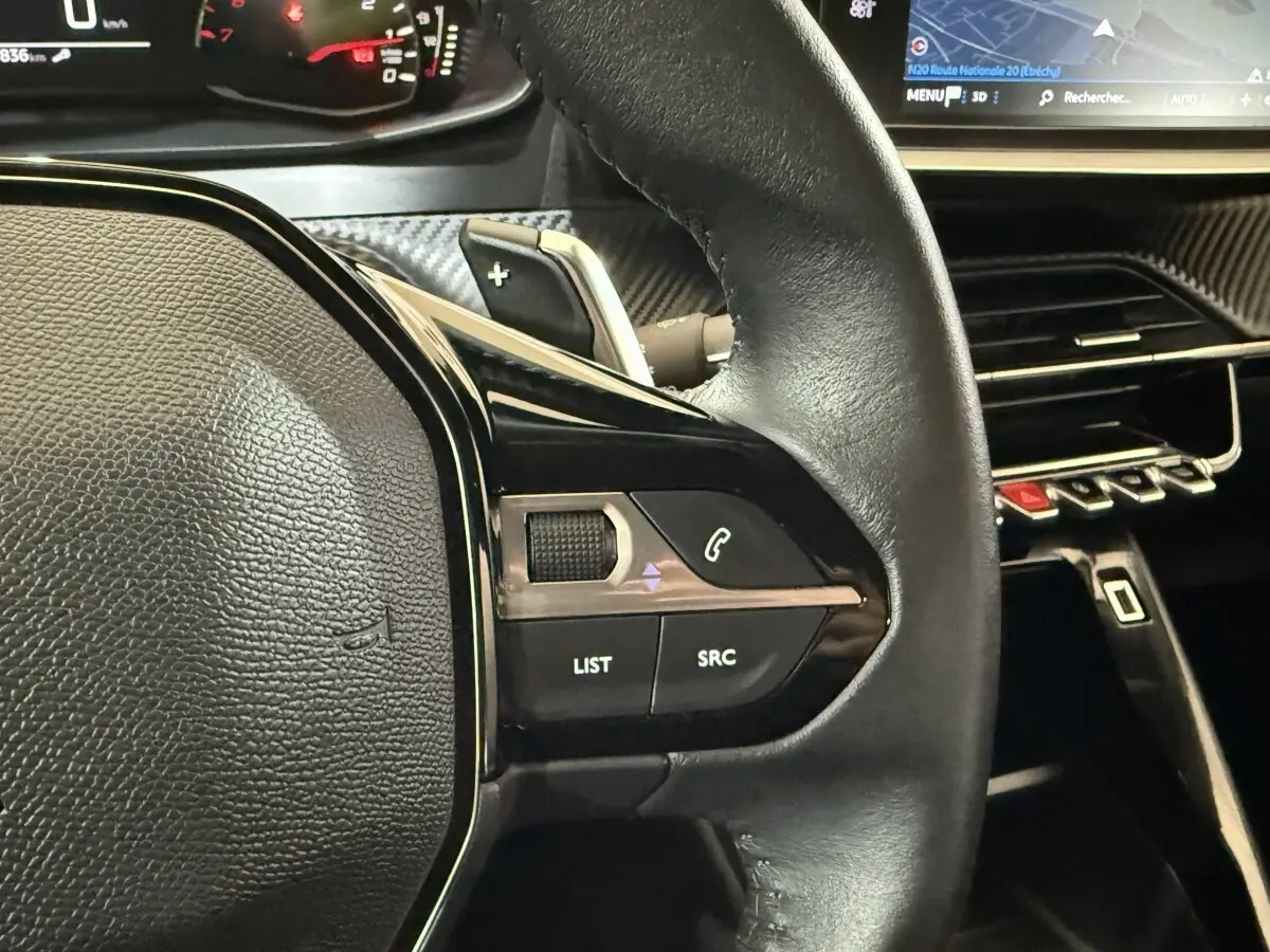 Gros plan sur le volant cuir noir du Peugeot 2008 2021, avec commandes audio et écran tactile du tableau de bord visible.