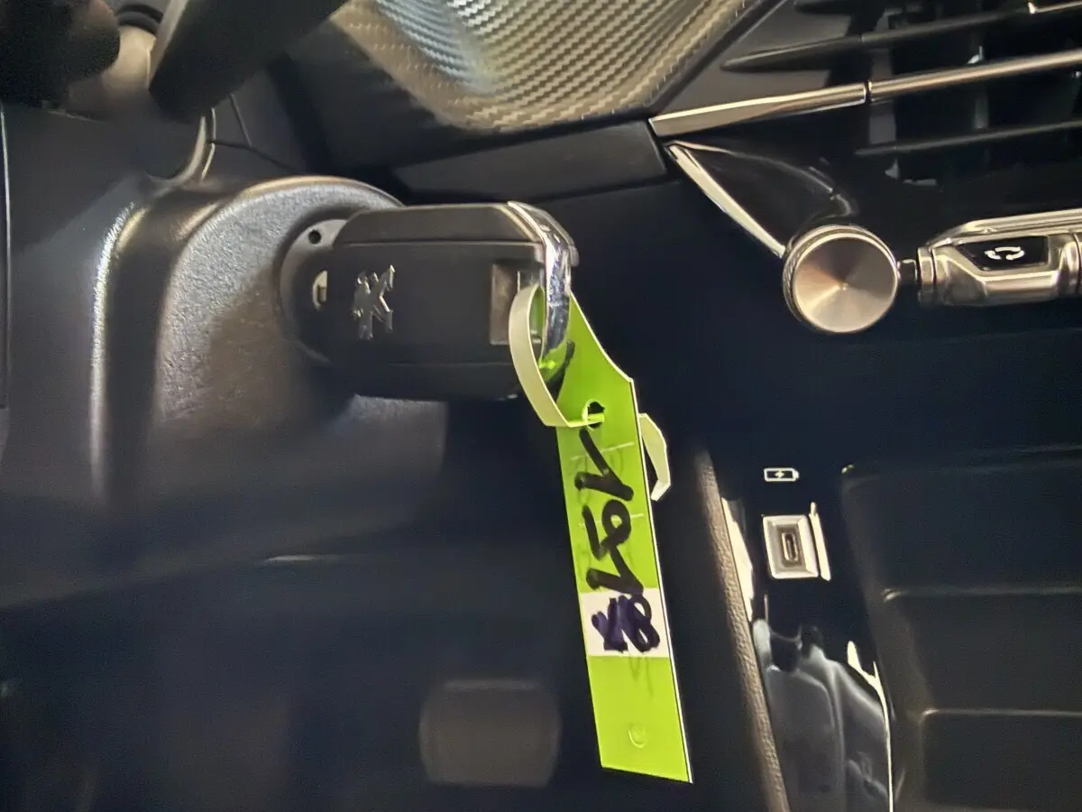 Gros plan intérieur sur la clé de contact Peugeot 2008 avec porte-clés vert, tableau de bord noir en arrière-plan.