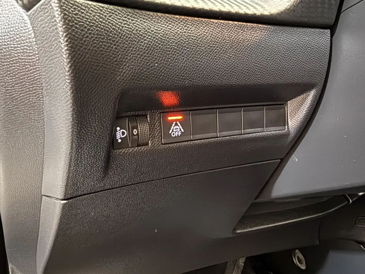 Détail du tableau de bord noir côté gauche avec commande d'éclairage et bouton d'alerte de franchissement de ligne allumé sur Peugeot 2008.