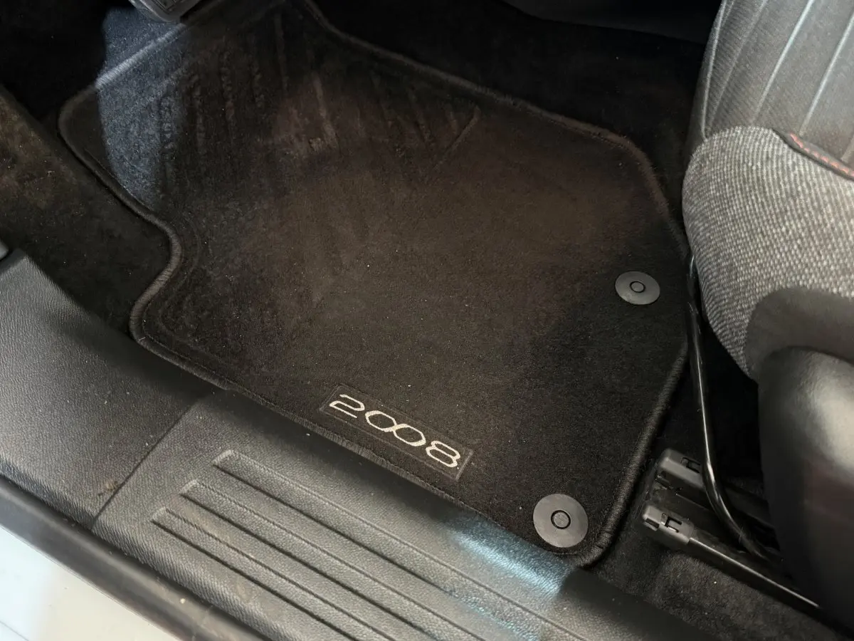 Tapis de sol noir avec logo 2008 côté conducteur dans l'habitacle d'une Peugeot 2008 blanche, vue rapprochée.