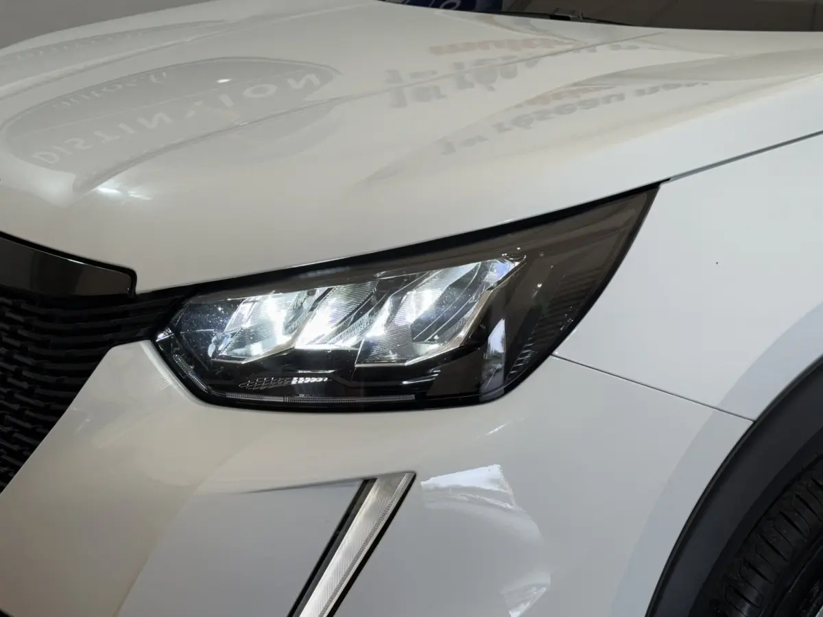 Gros plan sur le phare avant droit LED du Peugeot 2008 blanc, mettant en valeur la calandre et la carrosserie lisse.