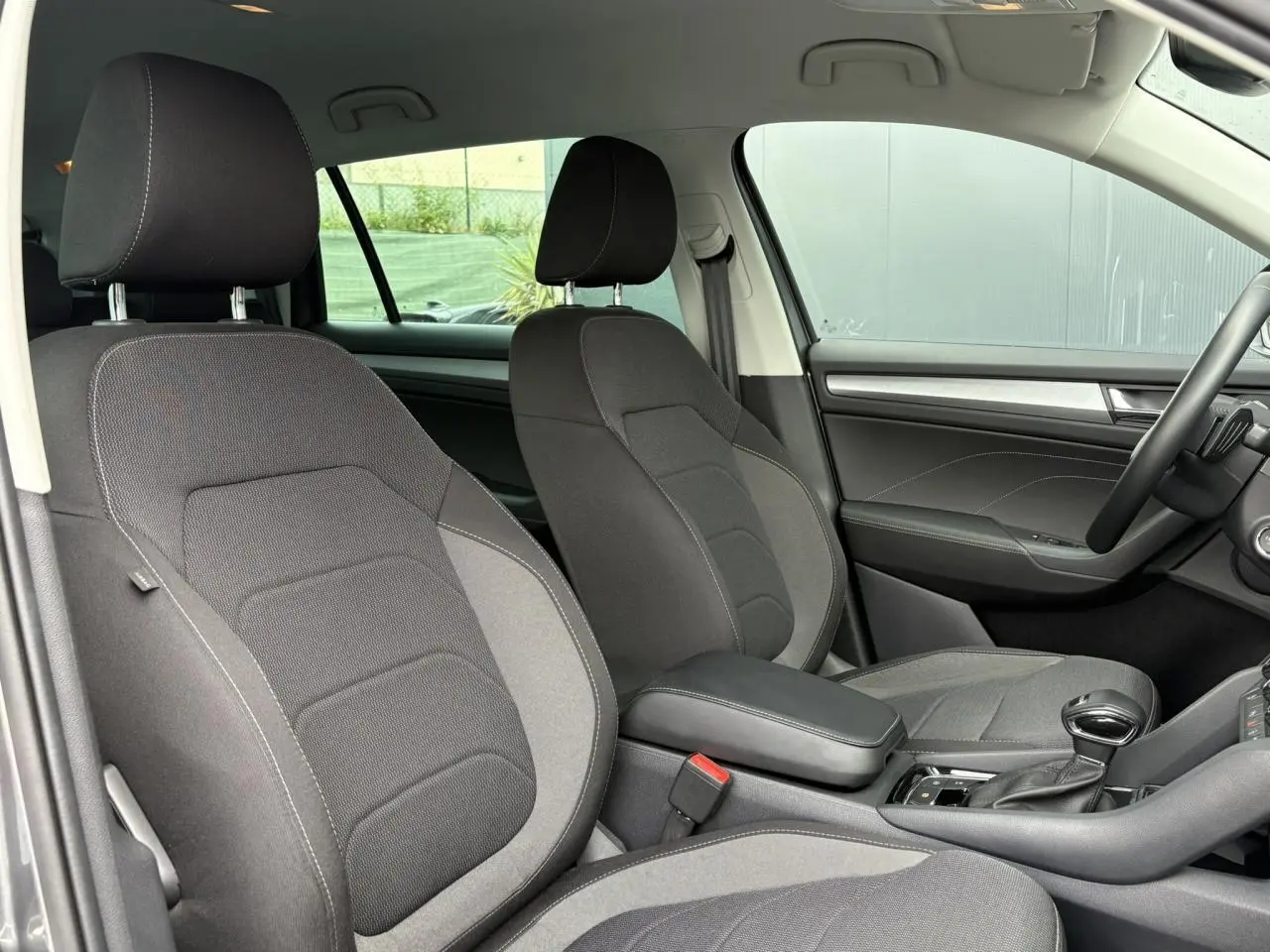 Vue intérieure côté avant droit du Skoda Kodiaq 2024, sièges tissu gris foncé avec accoudoir central noir.
