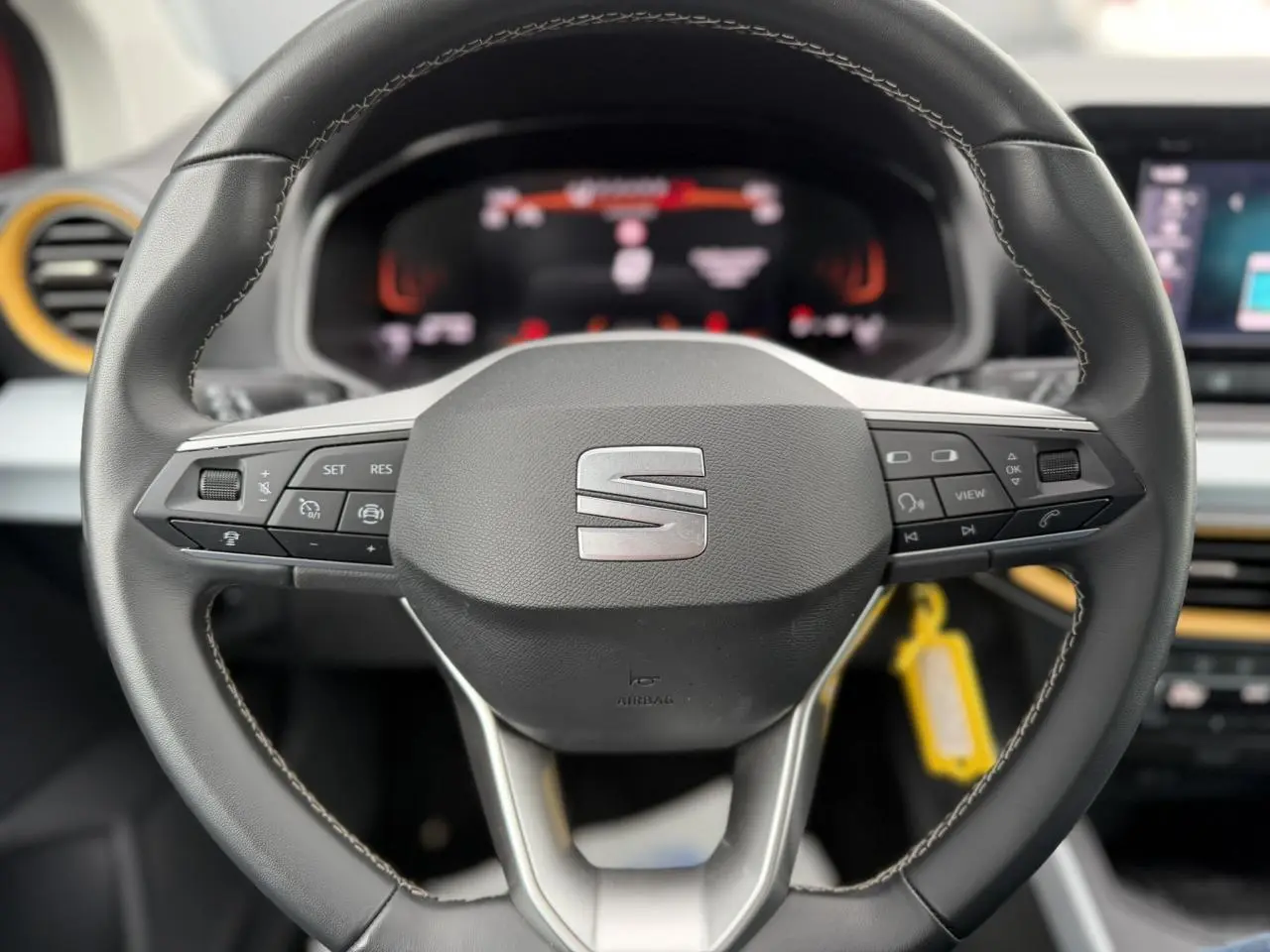 Gros plan sur le volant noir du SEAT Arona 2025 avec commandes intégrées et tableau de bord digital flou en arrière-plan.