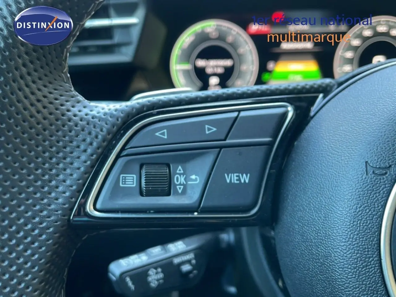 Gros plan sur les commandes à gauche du volant perforé d'une Audi A3 Sportback noire, avec affichage numérique en arrière-plan.