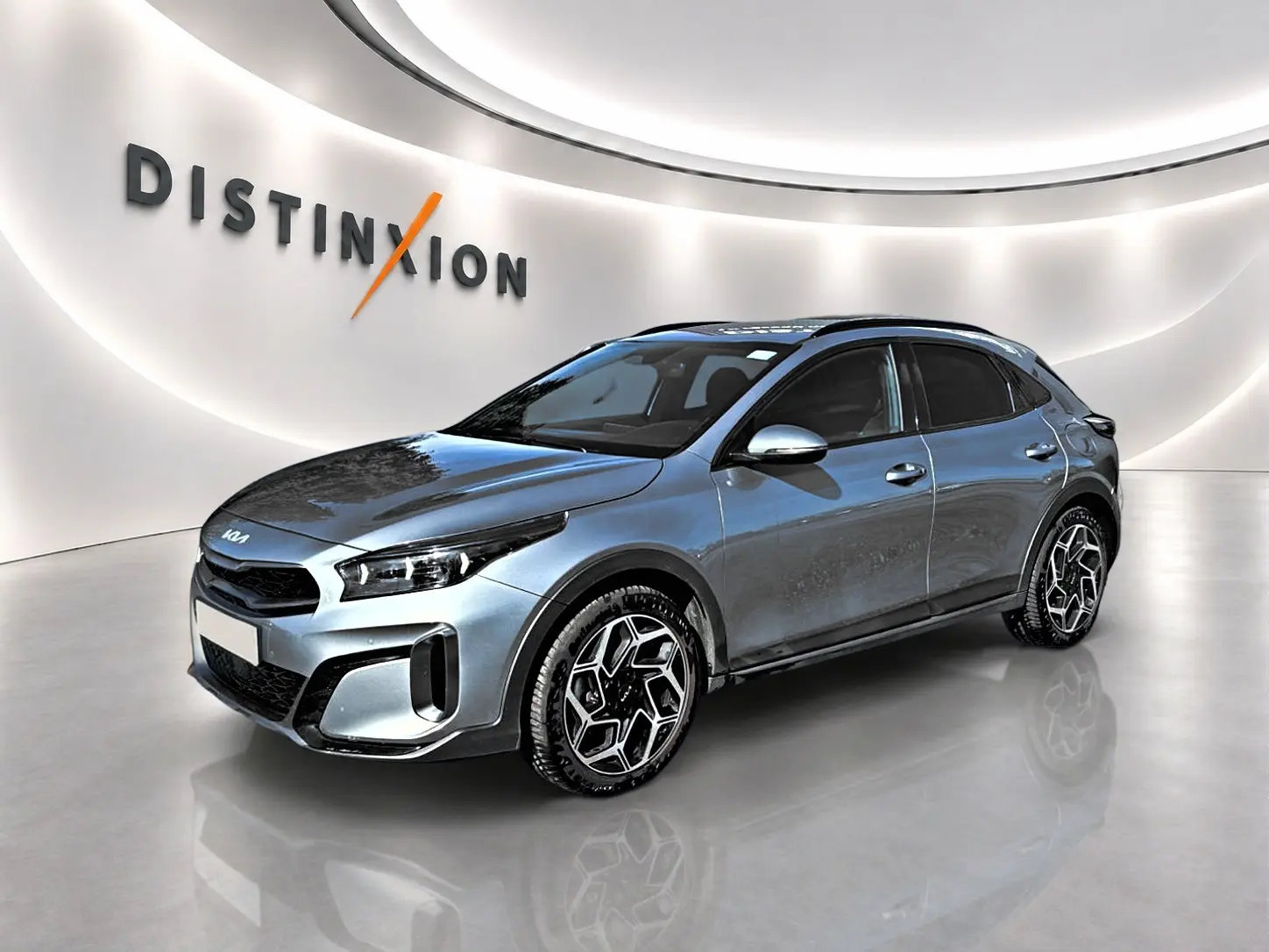 KIA Xceed gris en vue 3/4 avant droit, avec jantes alu distinctives et calandre chromée dans un showroom lumineux.