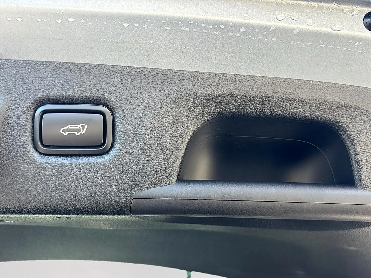 Bouton d'ouverture électrique du coffre sur panneau intérieur noir d'une KIA Xceed gris 3/4 arrière.