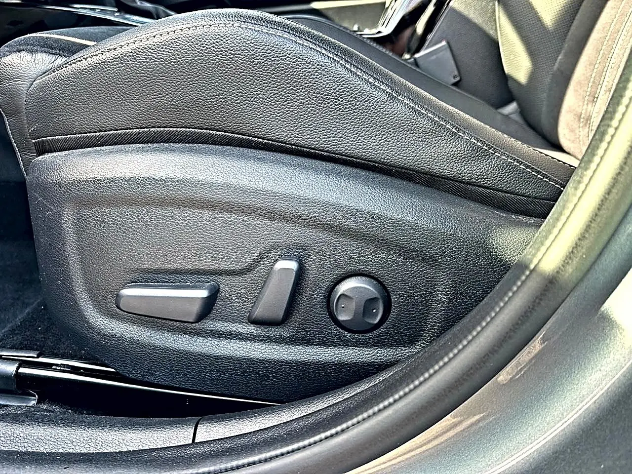 Gros plan sur les commandes électriques du siège conducteur en cuir noir du KIA Xceed gris 2024, côté gauche.