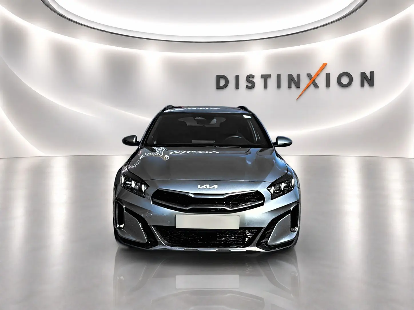 Vue avant d'un KIA Xceed gris 2024 avec calandre noire et phares LED dans un showroom lumineux.