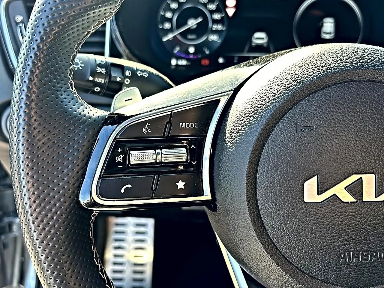 Gros plan sur le volant cuir perforé côté gauche du Kia Xceed gris, avec commandes multifonctions et palettes au volant.
