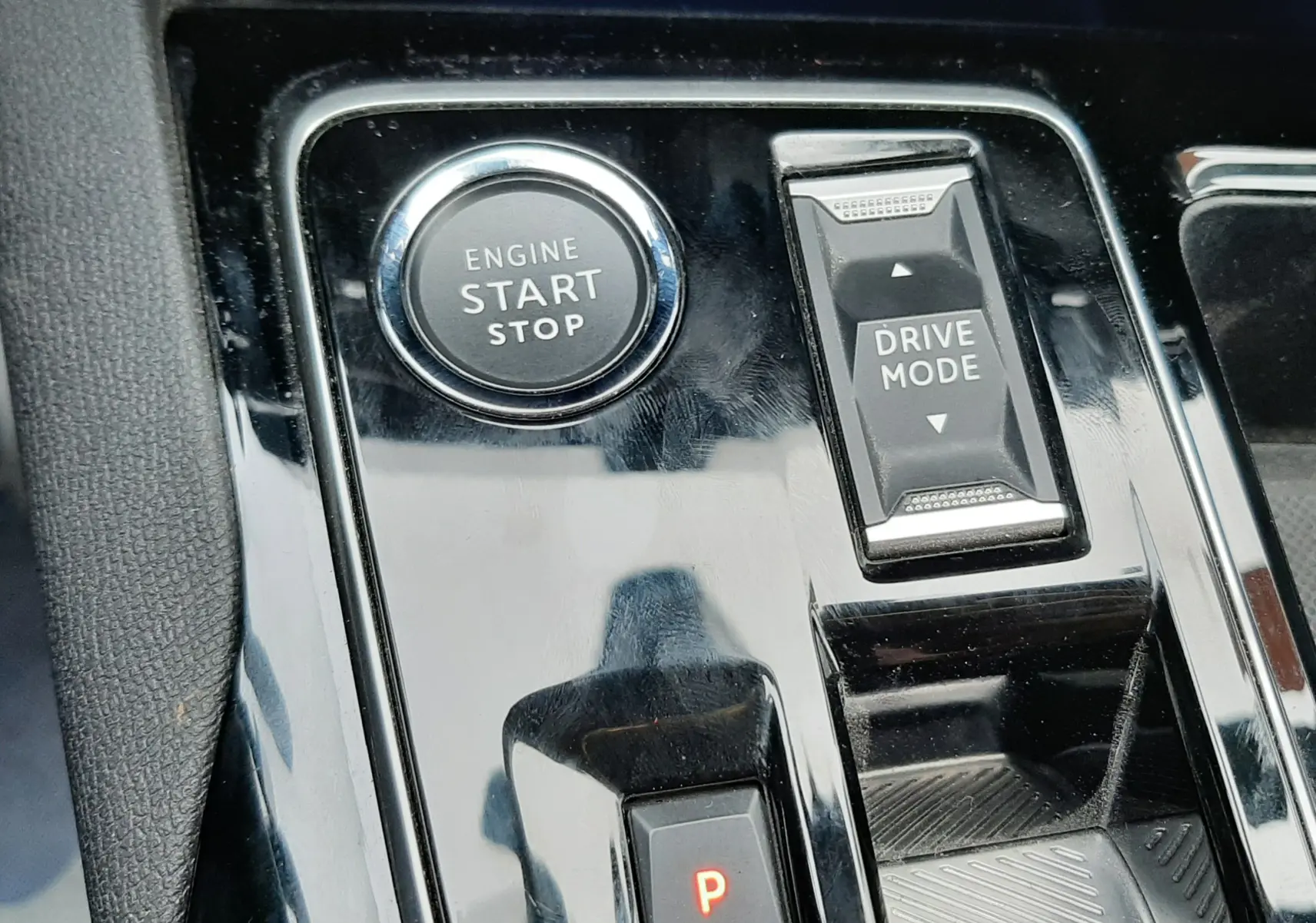 Gros plan sur la console centrale noire brillante du Peugeot 3008 Hybrid 136, avec bouton start/stop et sélecteur drive mode.