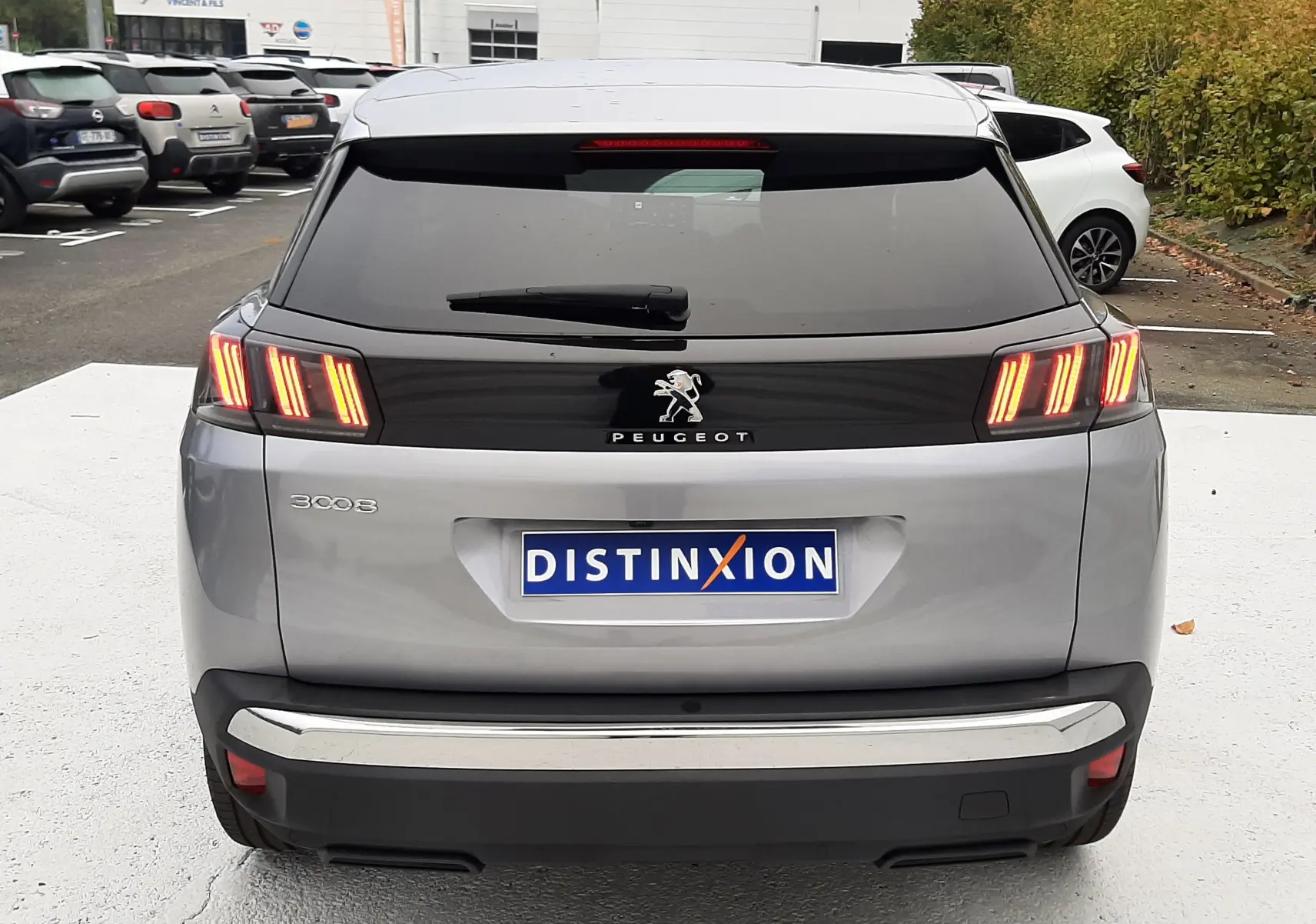 Vue arrière d'un Peugeot 3008 gris Artense avec feux arrière allumés sur un parking extérieur.