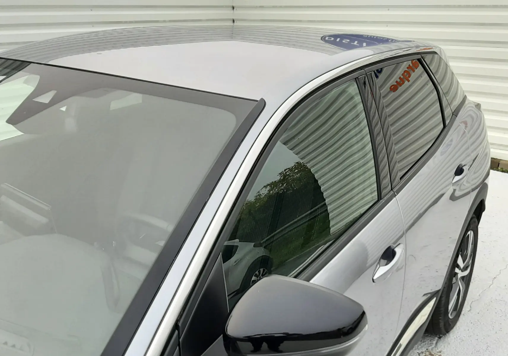 Vue en plongée du côté gauche avant d'un Peugeot 3008 Hybrid gris Artense avec rétroviseur noir brillant et vitres teintées.