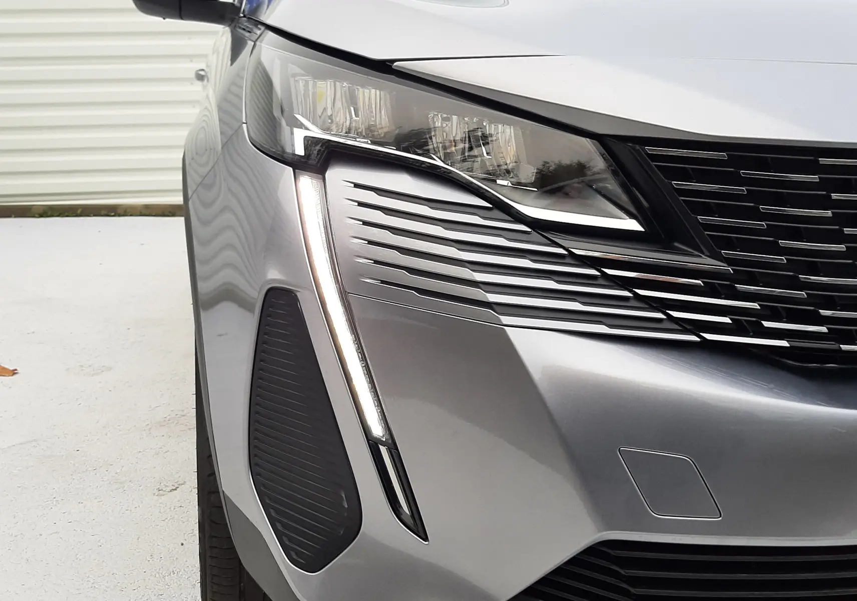 Gros plan sur l'avant gauche du Peugeot 3008 Hybrid gris Artense, mettant en valeur son phare LED et la calandre noire.