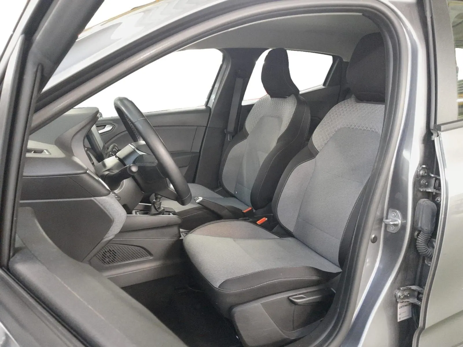 Vue intérieure côté conducteur de la Renault Clio V gris schiste, sièges textile gris à motif 3D et volant textile grainé.