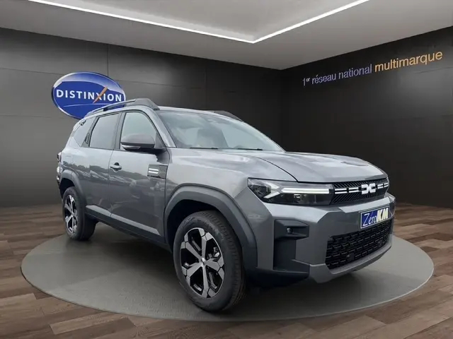 SUV Dacia Bigster gris foncé en 3/4 avant droit, avec calandre distinctive et jantes modernes, en showroom intérieur.