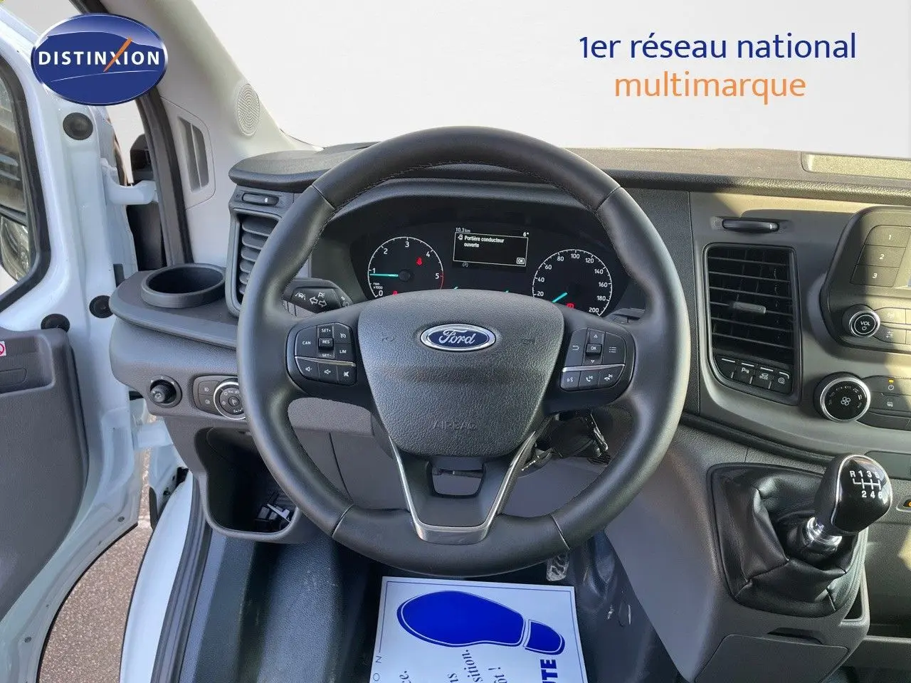 Vue intérieure centrée sur le volant et le tableau de bord du Ford Transit Fourgon blanc 2023 avec boîte manuelle.