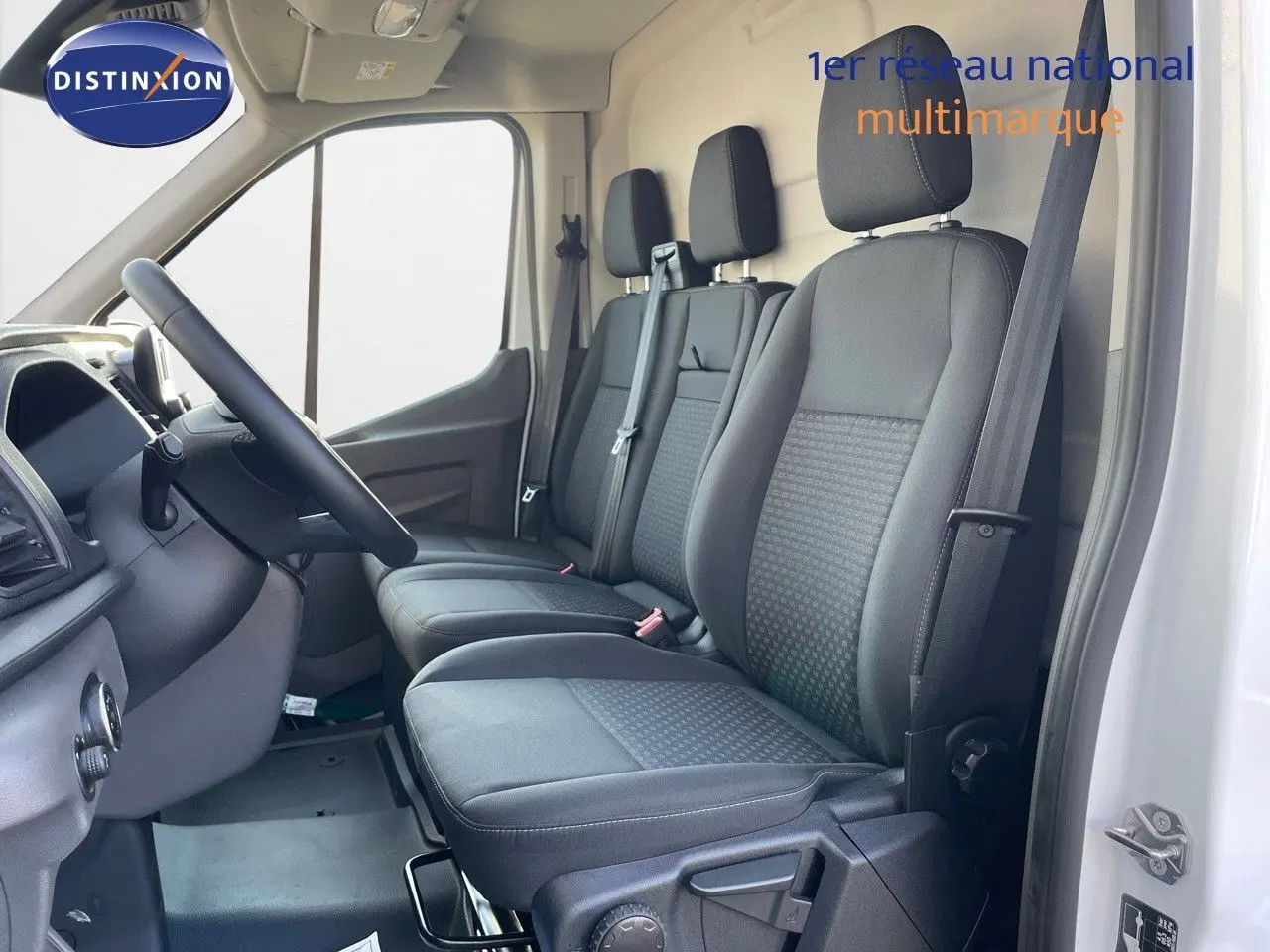 Vue intérieure côté conducteur du Ford Transit Fourgon blanc 2023 avec sièges tissu gris et volant noir.