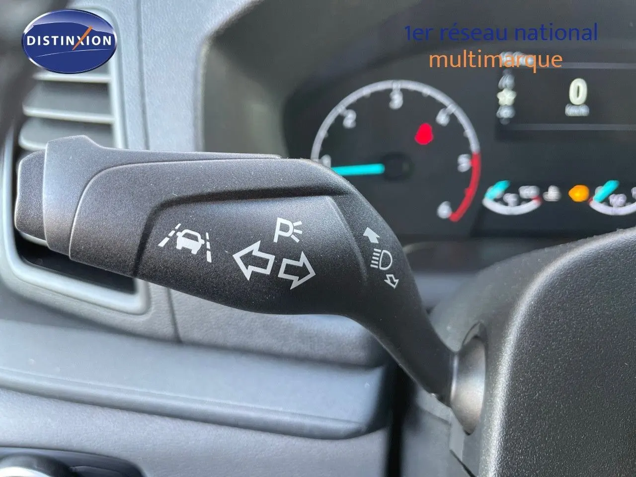 Gros plan sur la commande de clignotant du Ford Transit Fourgon blanc, avec tableau de bord en arrière-plan flou.