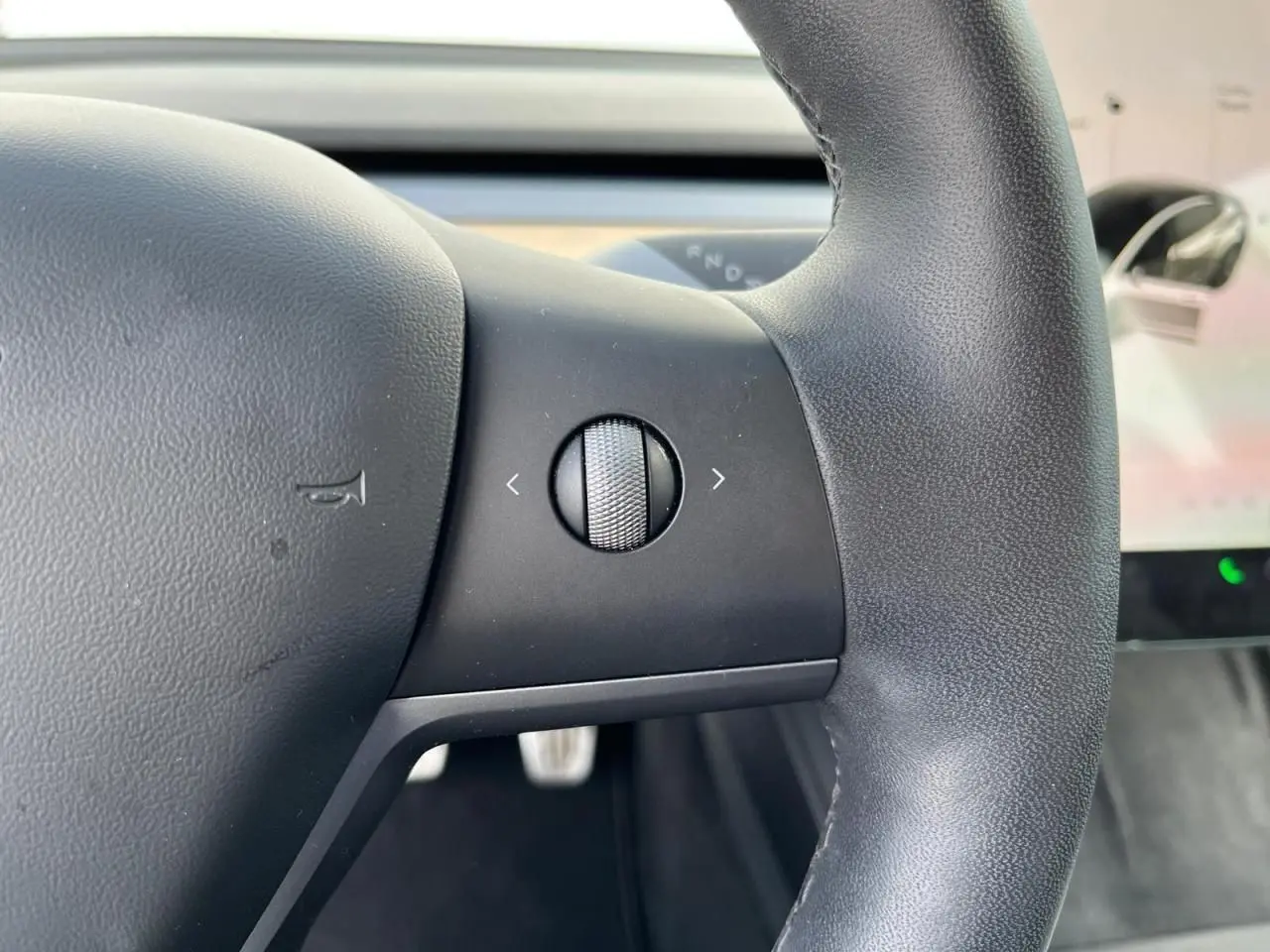Gros plan sur la molette de commande à gauche du volant noir d'une Tesla Model 3 blanche, intérieur moderne visible.
