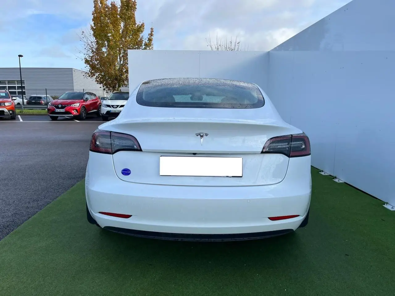 Vue arrière d'une Tesla Model 3 blanche 2022 avec feux arrière sombres et pare-chocs ton caisse.