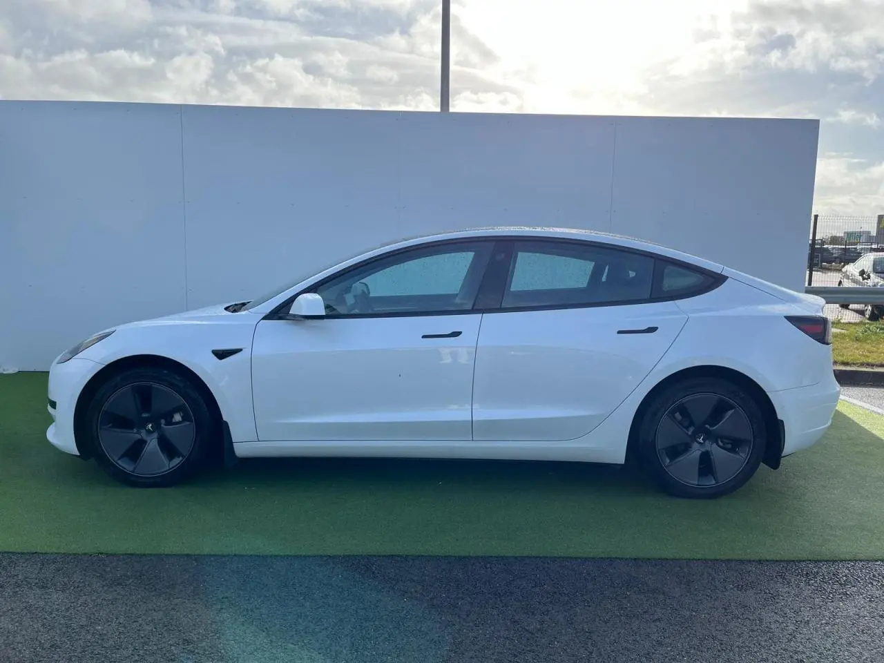 Profil côté gauche d'une Tesla Model 3 blanche 2022 avec jantes noires et poignées affleurantes ton carrosserie.