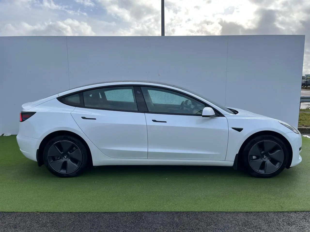Profil côté gauche d'une Tesla Model 3 blanche 2022 avec jantes noires et poignées affleurantes ton carrosserie.