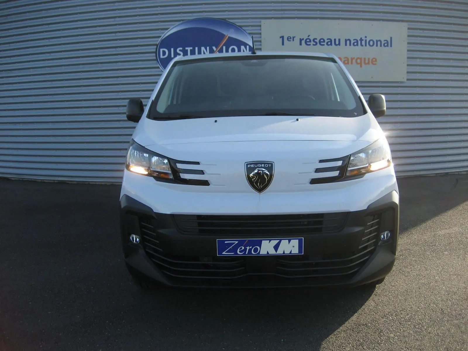 Vue frontale d'un Peugeot Expert Fourgon blanc 2025 avec phares allumés et logo lion visible sur la calandre.