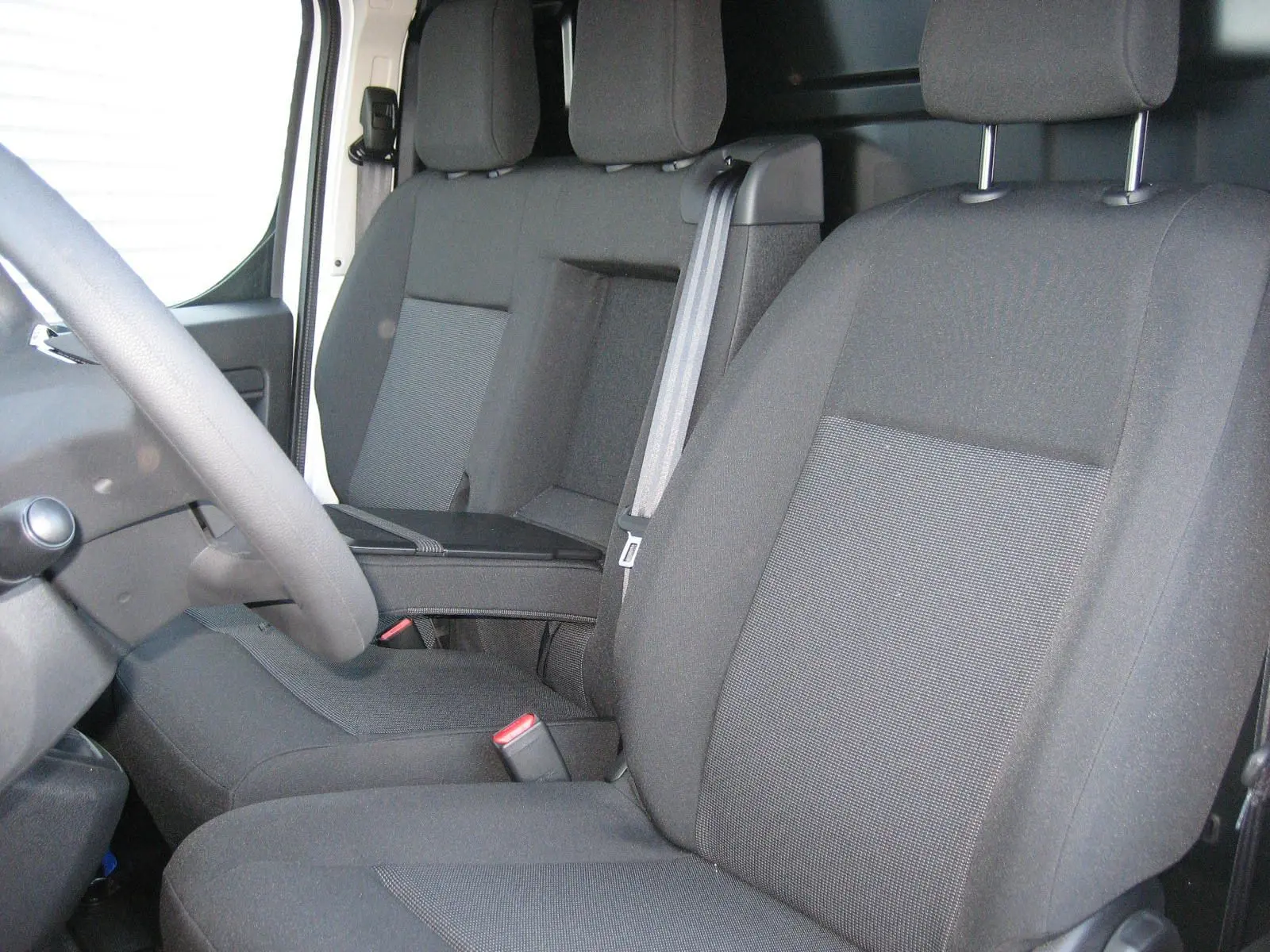 Vue intérieure rapprochée des sièges avant noirs du Peugeot Expert Fourgon avec accoudoir central et ceinture de sécurité.
