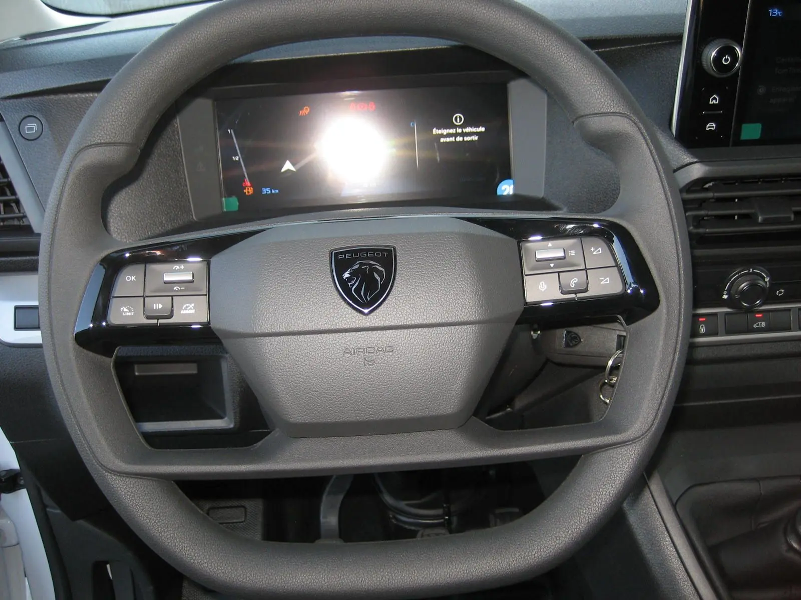 Vue rapprochée du volant gris foncé du Peugeot Expert Fourgon 2025 avec commandes intégrées et écran digital en arrière-plan.