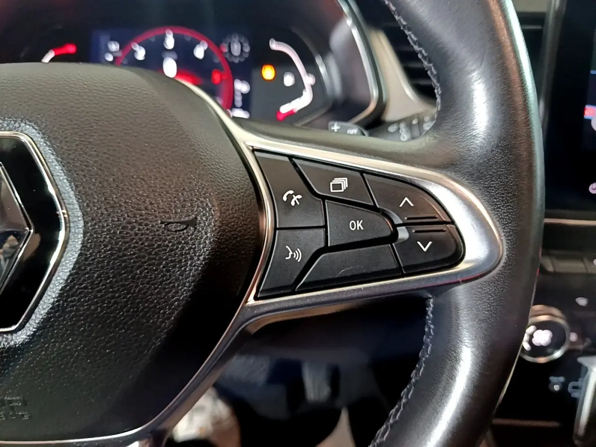 Gros plan sur la partie droite du volant cuir noir du Renault Captur jaune, avec commandes multifonctions et tableau de bord en arrière-plan.