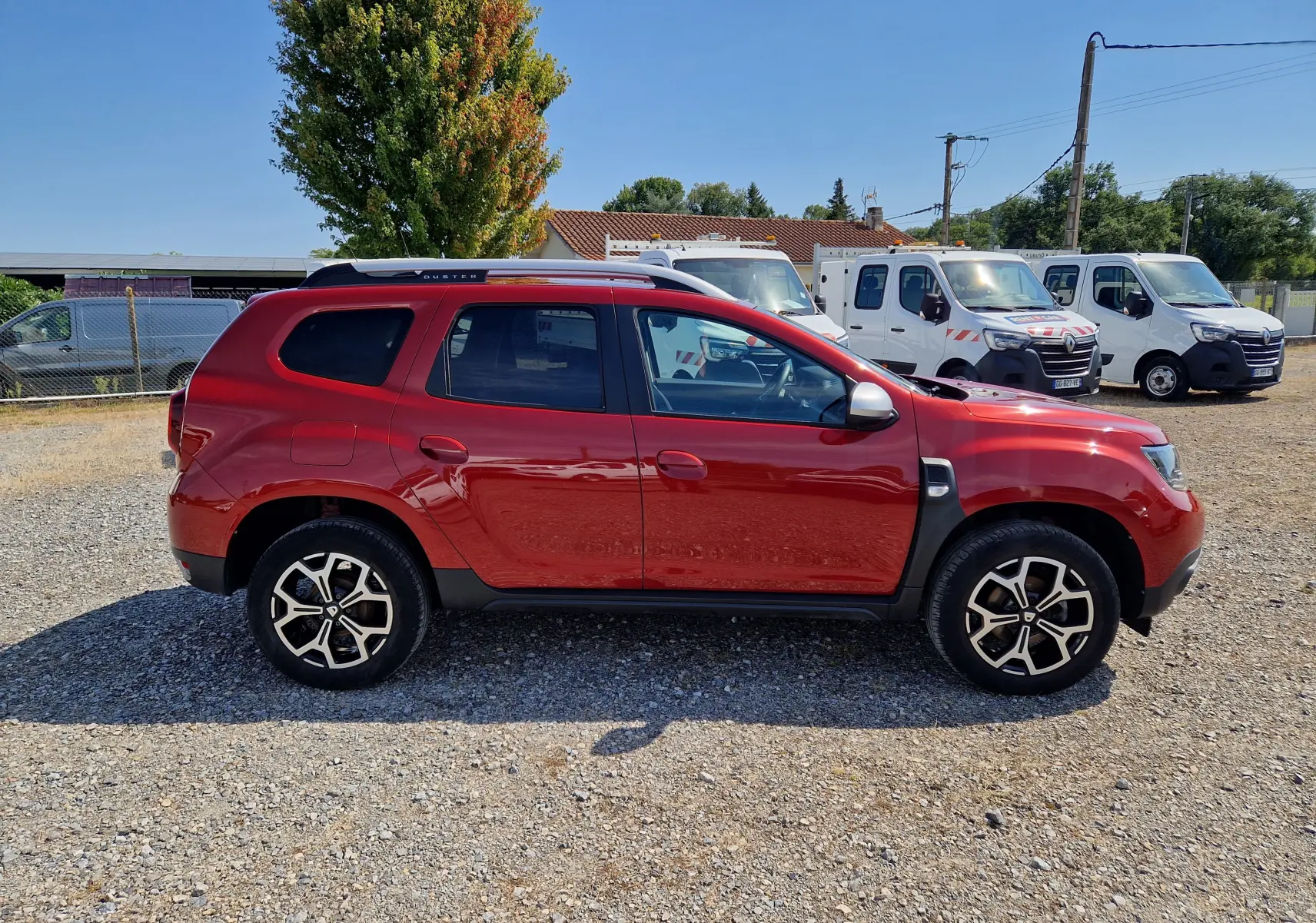 Profil droit d'un Dacia Duster rouge fusion 2021 avec jantes alliage noires et barres de toit argentées.