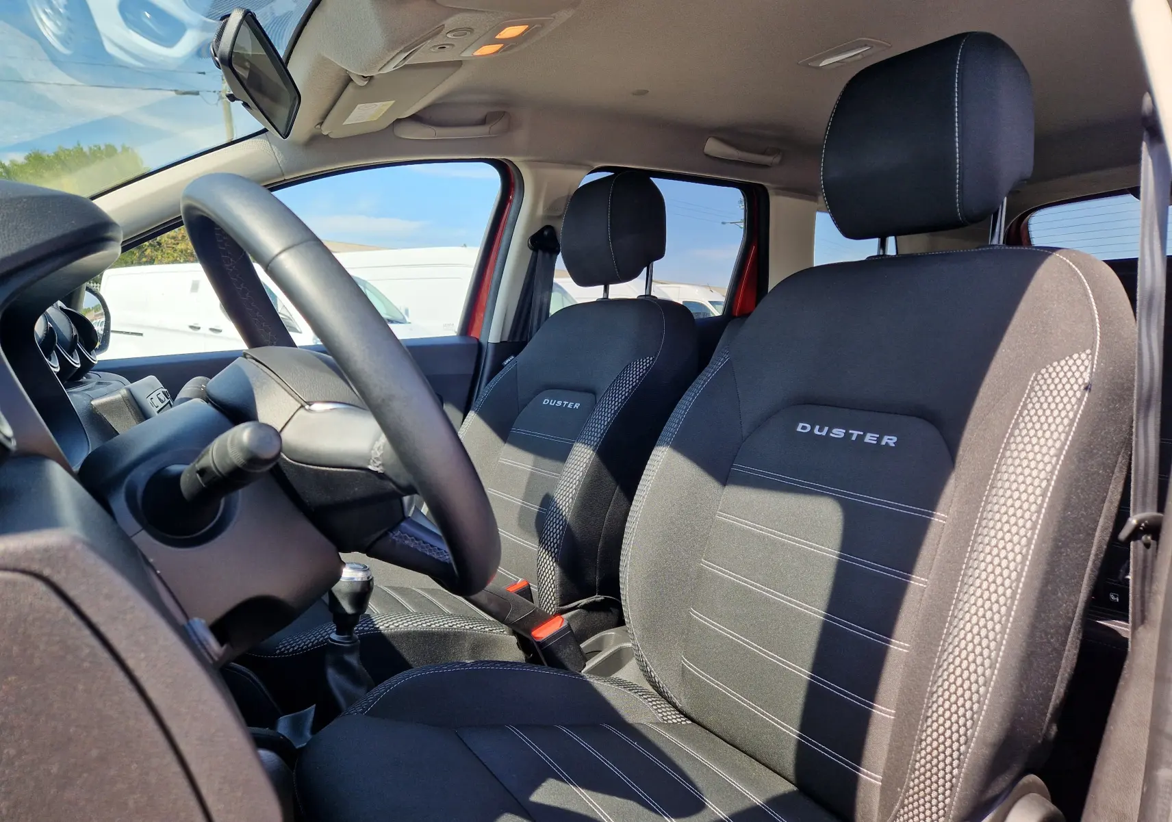 Vue intérieure côté conducteur du Dacia Duster 2021 rouge fusion, mettant en valeur les sièges noirs avec logo DUSTER brodé.