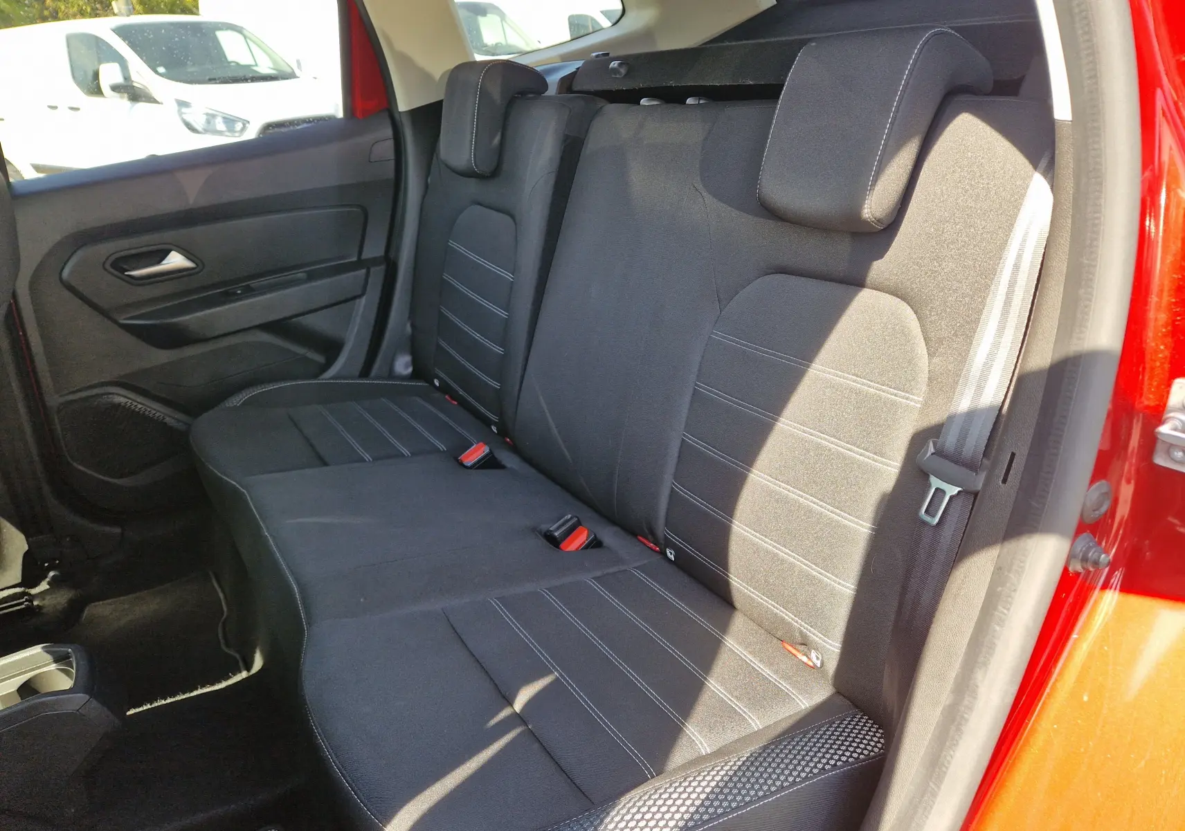Vue intérieure côté droit des sièges arrière noirs du Dacia Duster rouge fusion 2021, montrant les appuie-têtes et ceinture de sécurité.