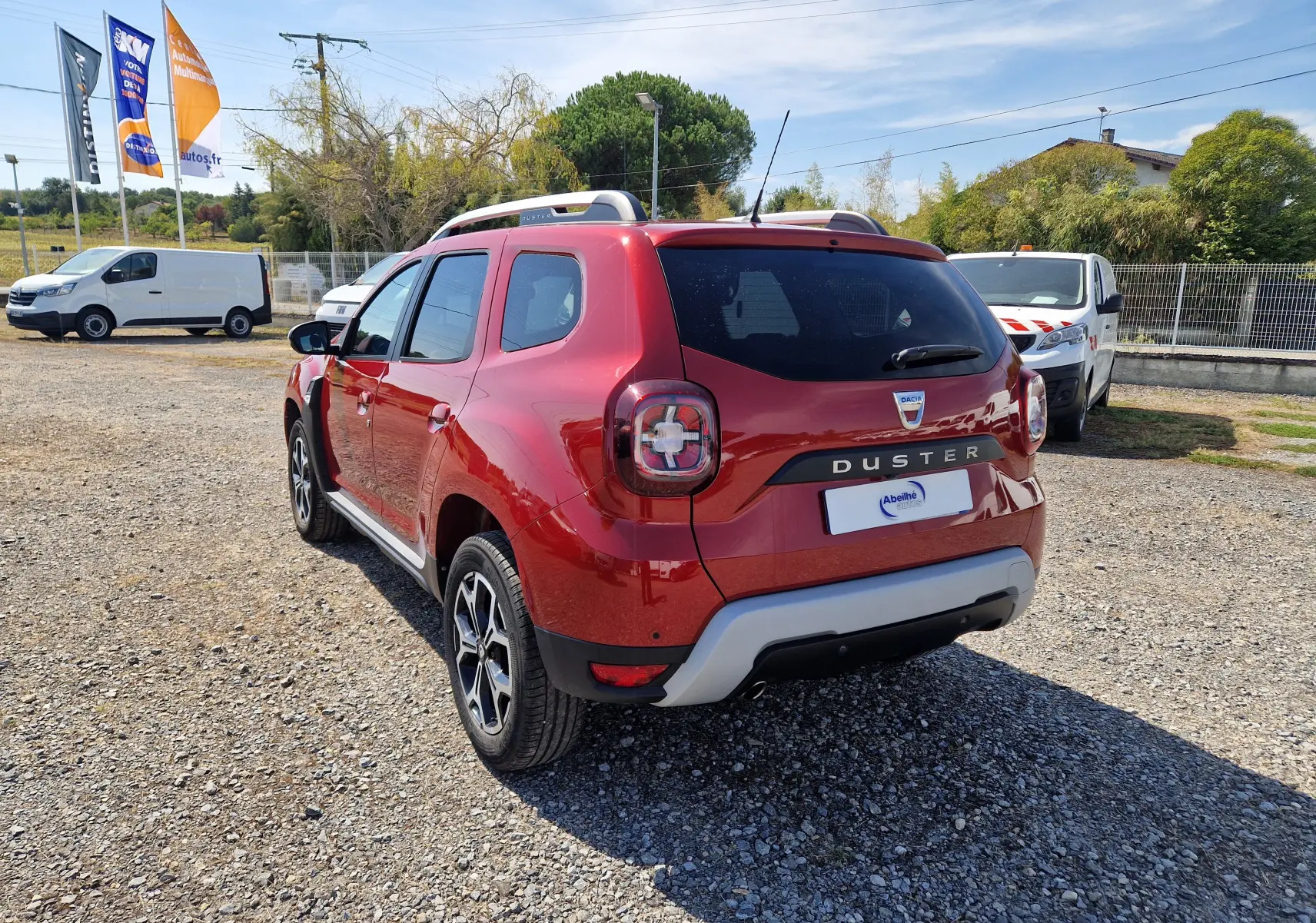 Vue 3/4 arrière droite d'un Dacia Duster rouge fusion 2021 avec jantes alliage et barres de toit visibles.