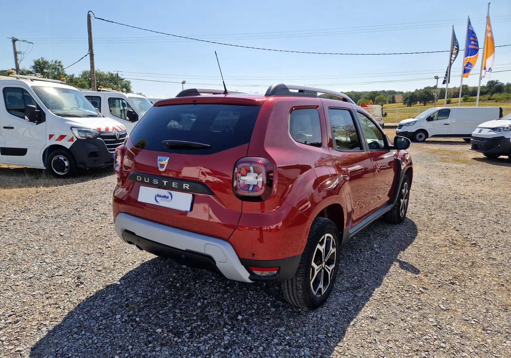 Vue 3/4 arrière droite du Dacia Duster rouge fusion 2021 avec jantes alliage et barres de toit visibles.