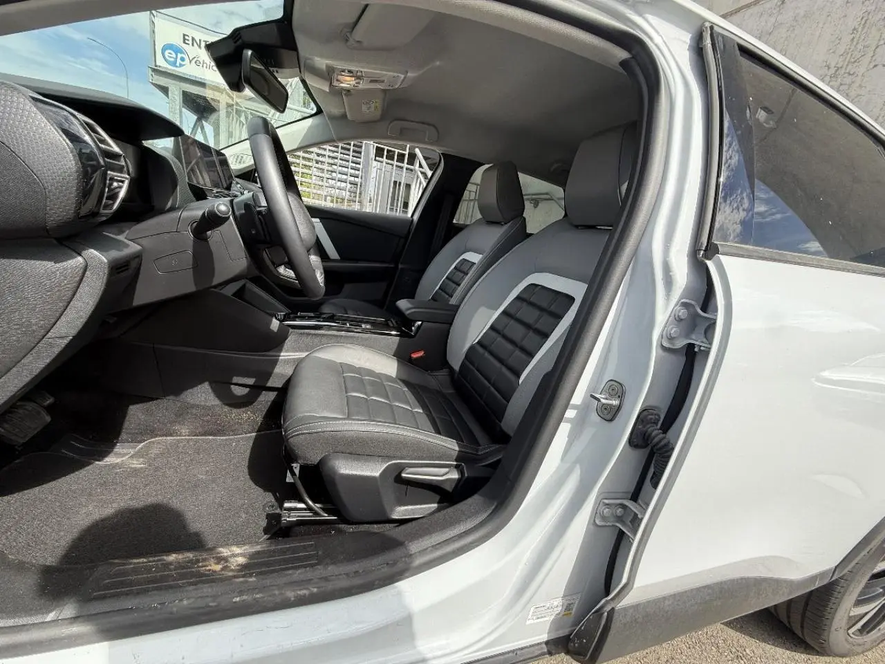 Vue intérieure côté conducteur d'une Citroën C4 blanc okenite 2025, sièges noirs avec inserts gris et tableau de bord moderne.
