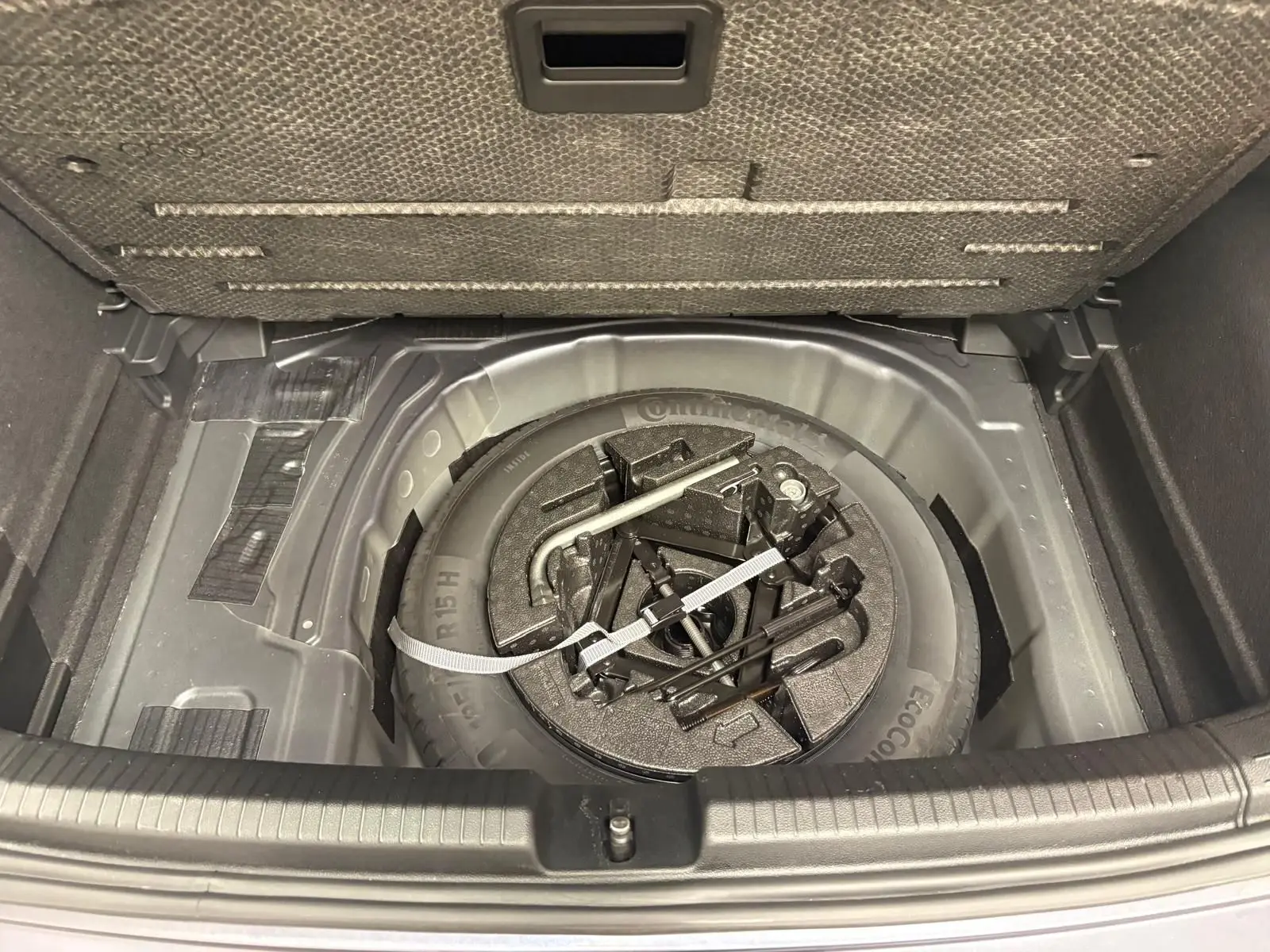 Coffre ouvert d’une Volkswagen Polo gris cendre 2024, montrant la roue de secours et les outils de dépannage rangés.