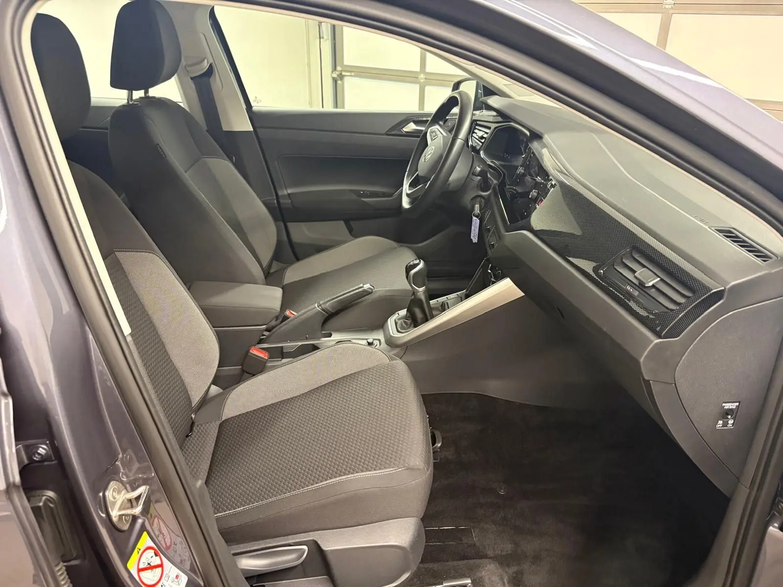 Vue intérieure côté conducteur de la Volkswagen Polo gris cendre 2024, avec sièges tissu et boîte manuelle visible.