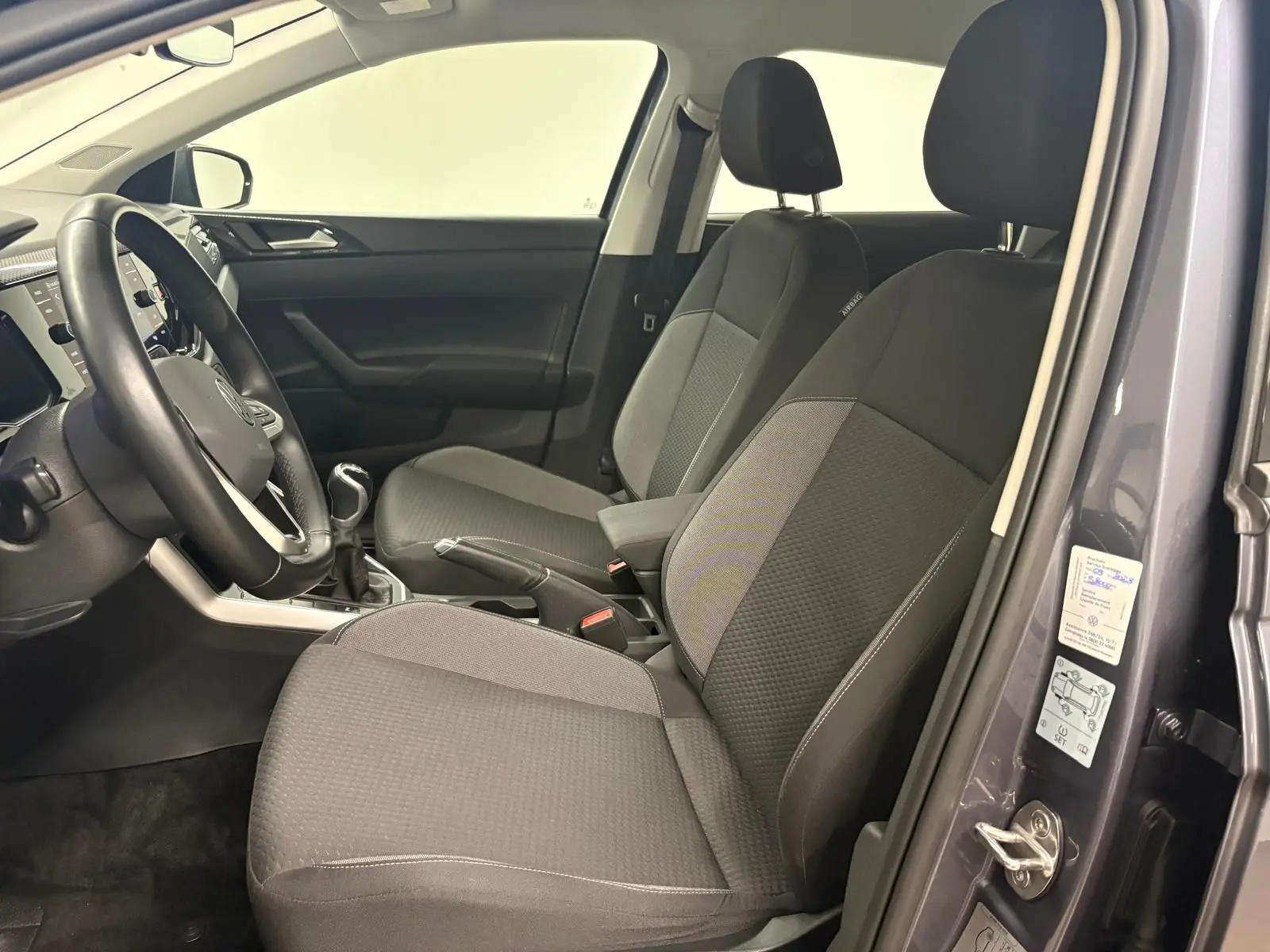 Vue intérieure côté conducteur de la Volkswagen Polo gris cendre 2024, montrant les sièges avant et la boîte manuelle.