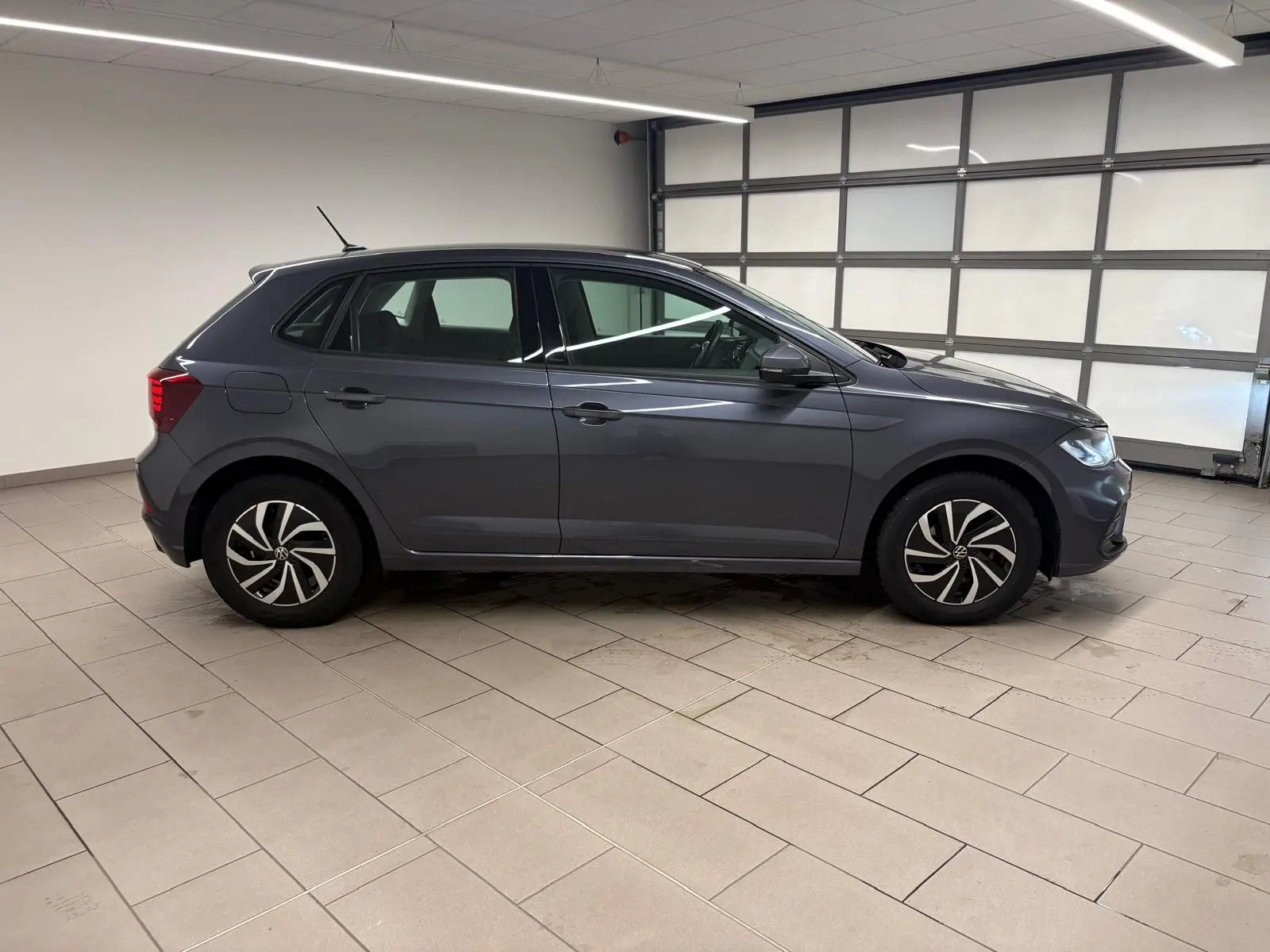 Vue de profil côté gauche d'une Volkswagen Polo gris cendre 2024 dans un garage lumineux avec jantes au design moderne.