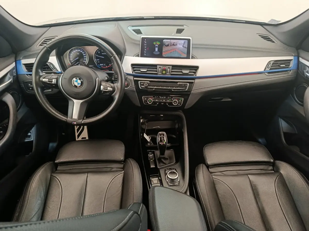 Vue intérieure avant du BMW X1 sDrive18i M Sport 2019, sièges cuir noirs et écran tactile affichant la caméra de recul.