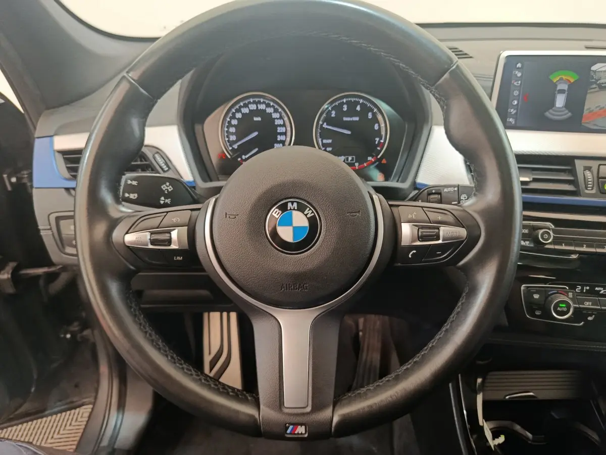 Volant cuir noir BMW M Sport avec commandes intégrées, tableau de bord et écran tactile affichant l'aide au stationnement.